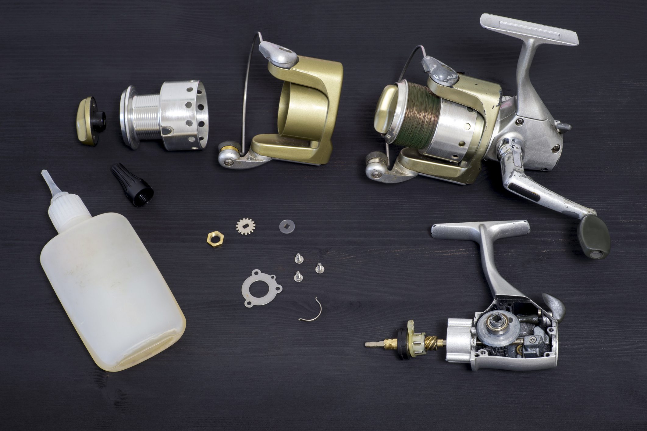 A fishing spinning reel as a whole and a second similar completely disassembled on a dark wooden background. Top view. fishing rod components