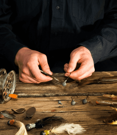 Person crafting fishing lures on wooden table.